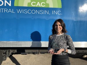 Sara holds her Aspire Award in front of a blue semi truck with the CACSCW logo on the side.