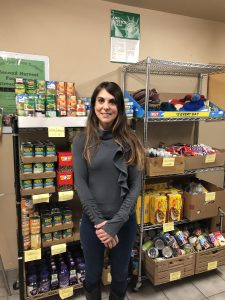 A participant poses in front of shelves stacked with canned food at the food pantry.
