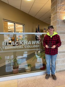Avery holds his Aspire Award while standing in front of a glass Blackhawk Technical College sign