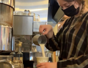 Young female pours milk into a to-go cup in a cafe kitchen