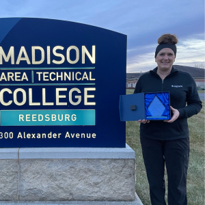 Melanie poses with an Aspire Award trophy by a Madison Area Technical College sign.