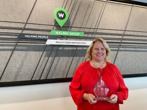 Tracey holds her Aspire Award in front of a wall with the Walbec Group logo on it.